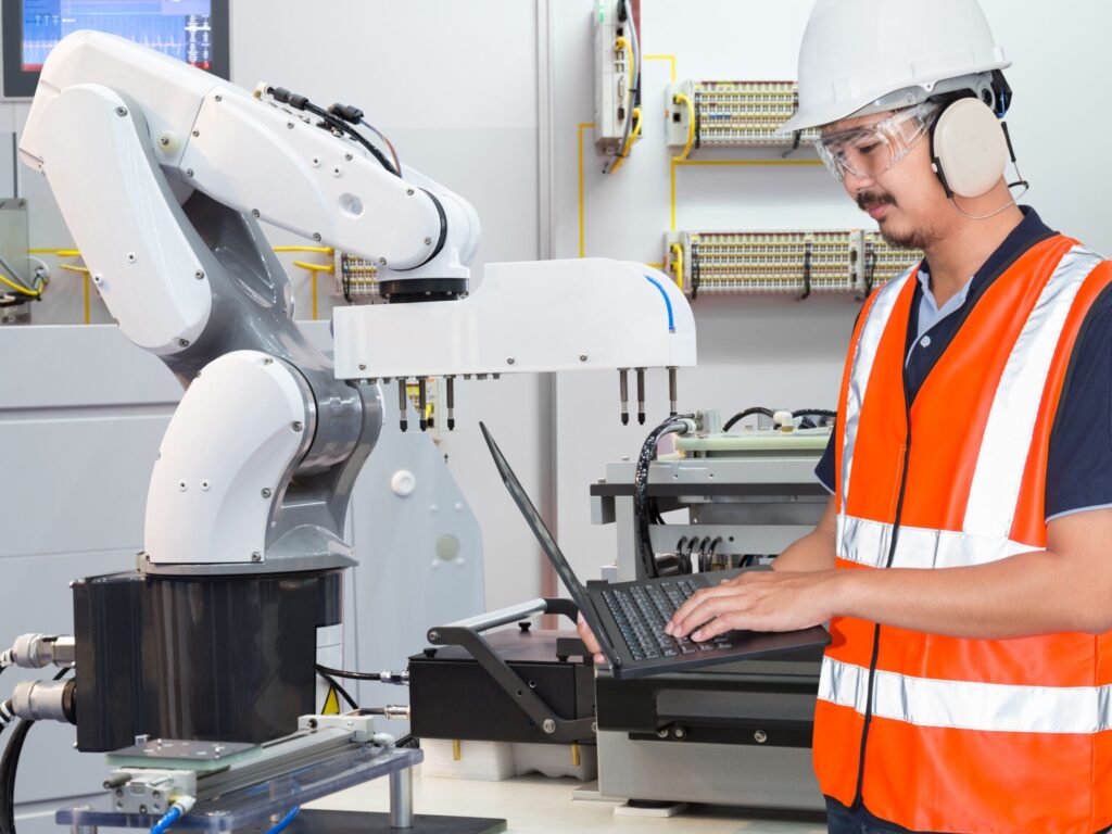 Engineer in safety gear programming a robotic arm on a manufacturing floor.