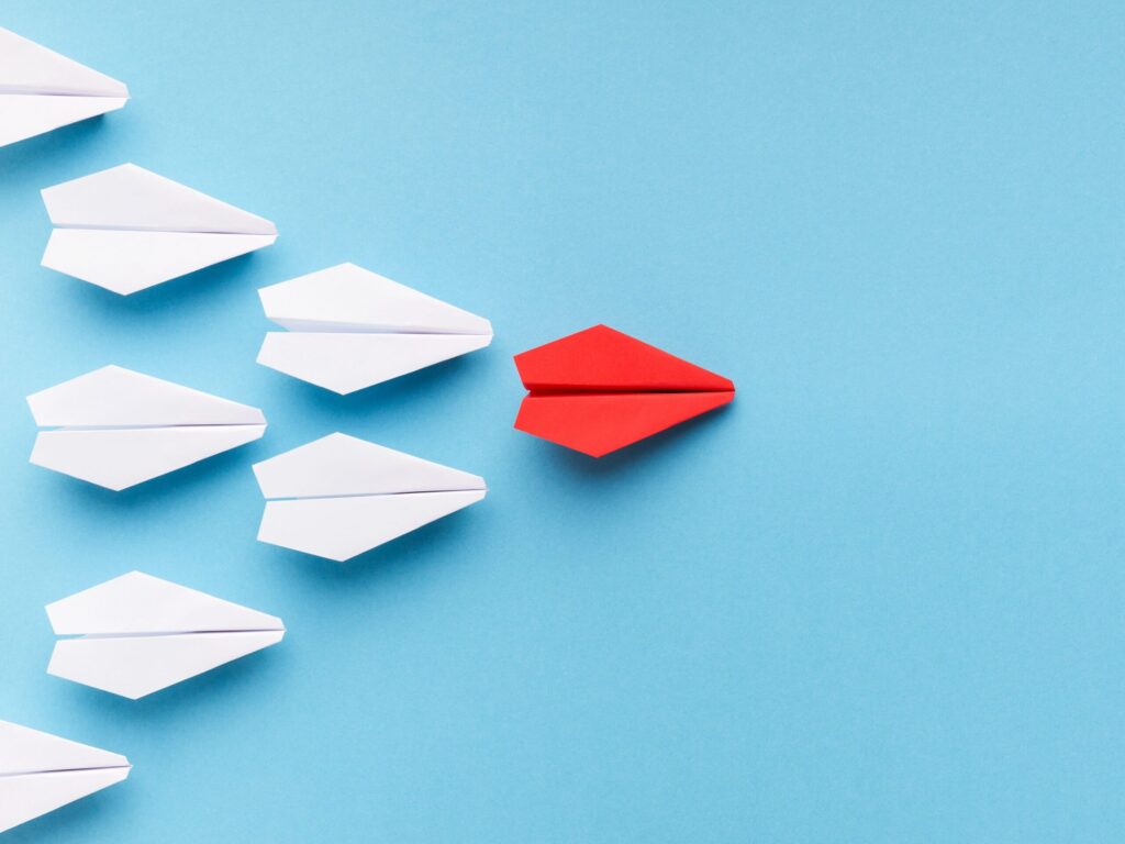 Red paper airplane flying ahead of white ones symbolizing leadership and initiative