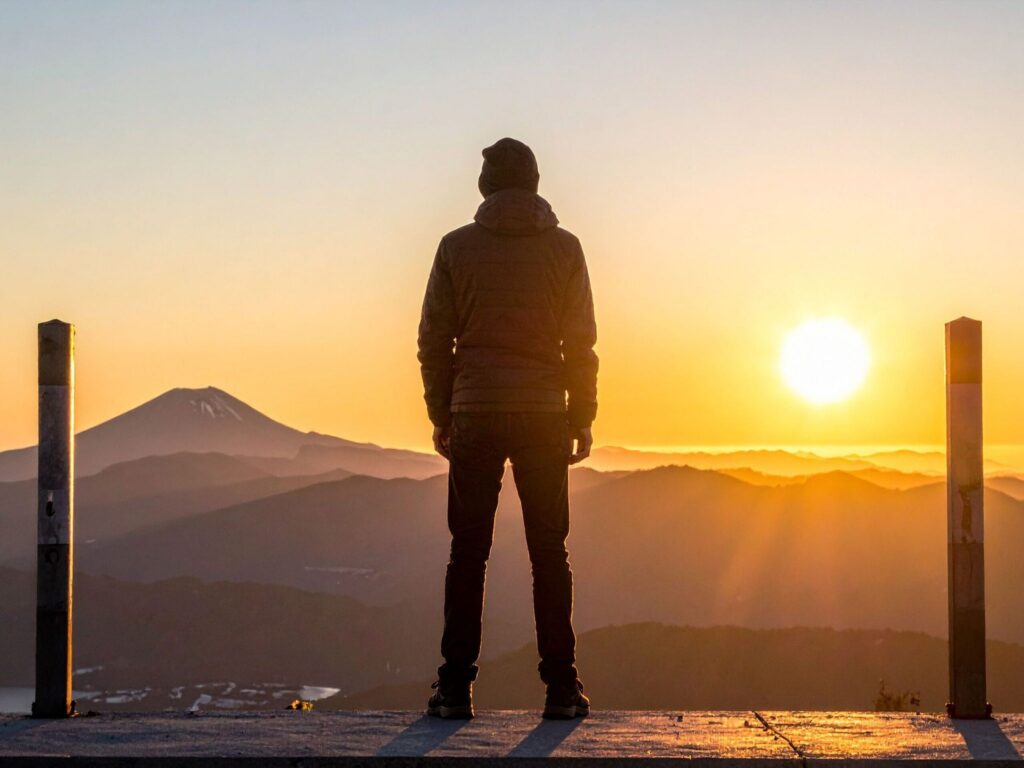 Person watching the sunset over distant mountains, symbolizing peace and fulfillment.
